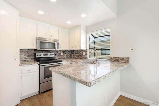 kitchen featuring sink, kitchen peninsula, white cabinets, and appliances with stainless steel finishes