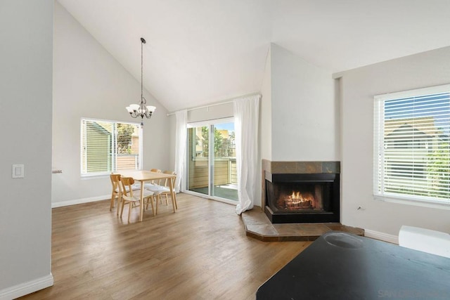 dining space with a tiled fireplace, hardwood / wood-style flooring, a notable chandelier, and high vaulted ceiling