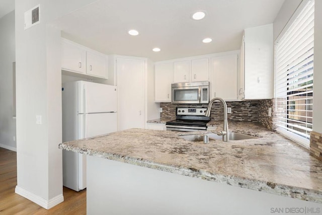 kitchen with sink, light wood-type flooring, appliances with stainless steel finishes, kitchen peninsula, and white cabinets