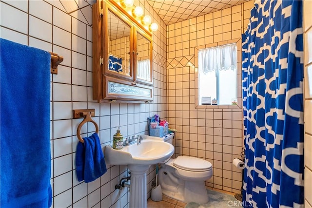 bathroom with tile patterned floors, toilet, sink, a shower with curtain, and tile walls