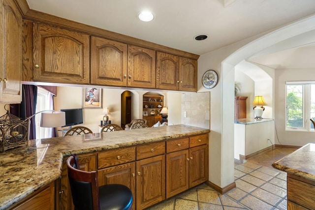 kitchen with light stone counters, kitchen peninsula, and decorative backsplash