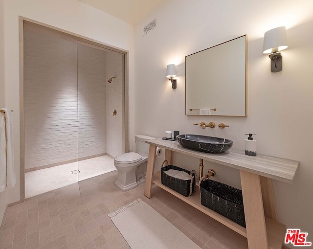 bathroom with sink, toilet, and a tile shower