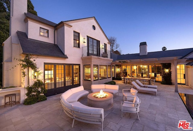 back house at dusk with a balcony, an outdoor living space with a fire pit, and a patio