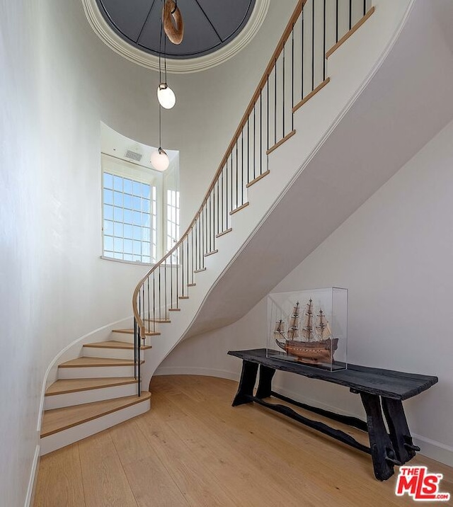 stairs featuring a high ceiling, crown molding, and wood-type flooring