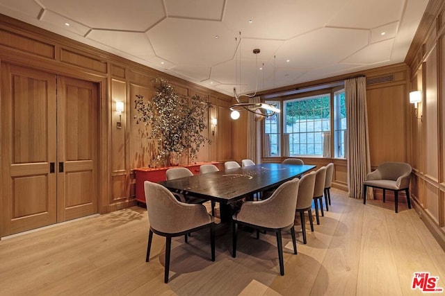 dining room featuring light wood-type flooring, wooden walls, and a notable chandelier