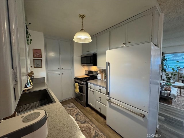 kitchen featuring appliances with stainless steel finishes, white cabinetry, sink, decorative light fixtures, and dark wood-type flooring