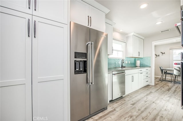 kitchen featuring light hardwood / wood-style flooring, sink, white cabinetry, decorative backsplash, and stainless steel appliances