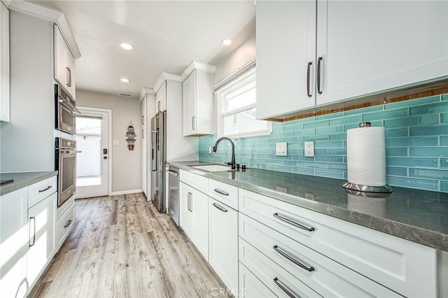 kitchen featuring light hardwood / wood-style floors, white cabinetry, dark stone counters, sink, and stainless steel appliances