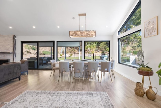 dining room with light hardwood / wood-style flooring, a stone fireplace, and vaulted ceiling