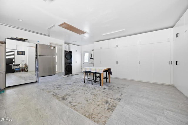 kitchen with stacked washer / drying machine, white cabinetry, stainless steel refrigerator, and a breakfast bar area