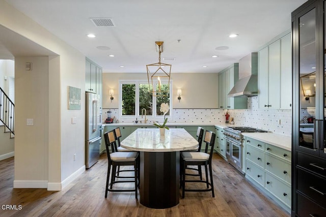 kitchen with a center island, high end appliances, wall chimney range hood, sink, and pendant lighting