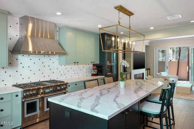 kitchen with dark wood-type flooring, light stone counters, wall chimney range hood, a kitchen island, and double oven range