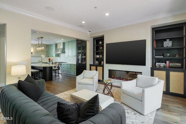 living room featuring built in shelves, crown molding, and light wood-type flooring