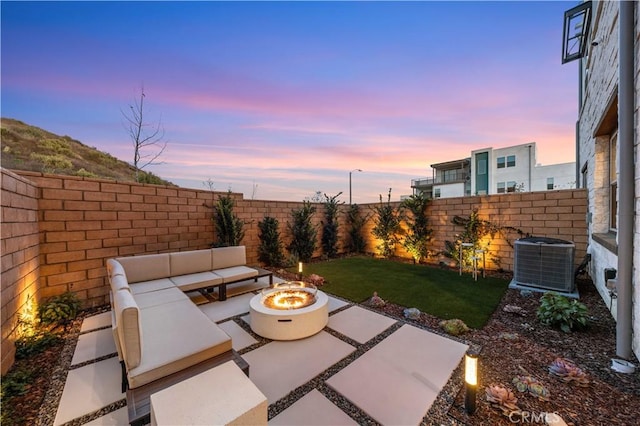 patio terrace at dusk featuring an outdoor living space with a fire pit, a lawn, and central air condition unit