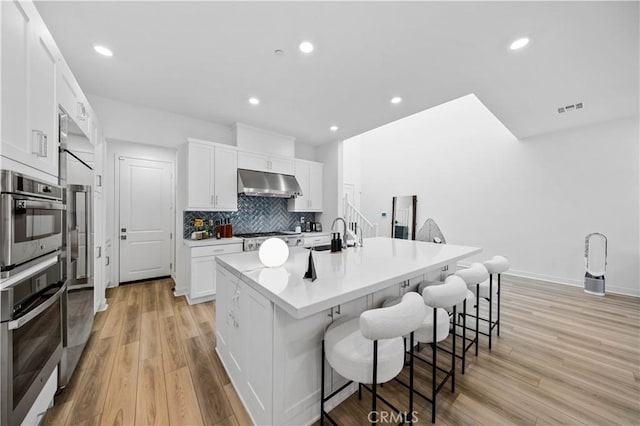 kitchen featuring light hardwood / wood-style floors, white cabinets, oven, and an island with sink