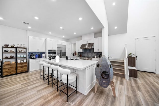 kitchen with built in fridge, white cabinetry, sink, backsplash, and a breakfast bar area