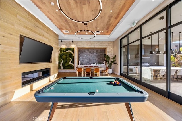 game room with light hardwood / wood-style floors, wooden ceiling, wooden walls, and a fireplace