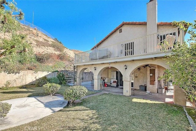 back of property featuring ceiling fan, a patio, a yard, and a balcony