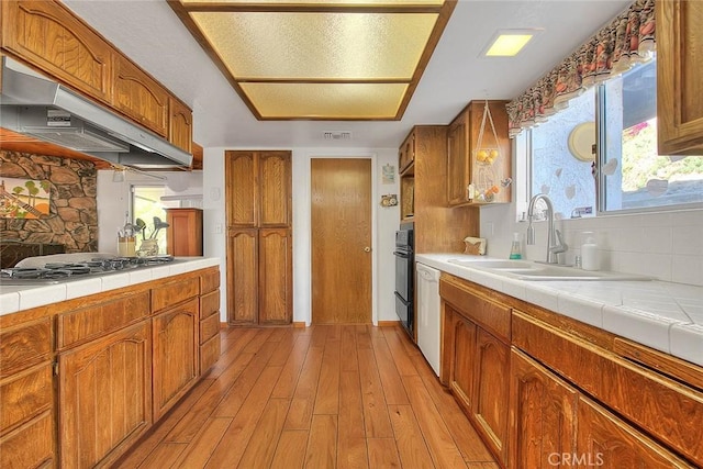 kitchen featuring black oven, light hardwood / wood-style floors, sink, stainless steel gas cooktop, and tile countertops