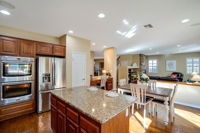 kitchen with a center island, a fireplace, dark hardwood / wood-style flooring, stainless steel appliances, and light stone counters