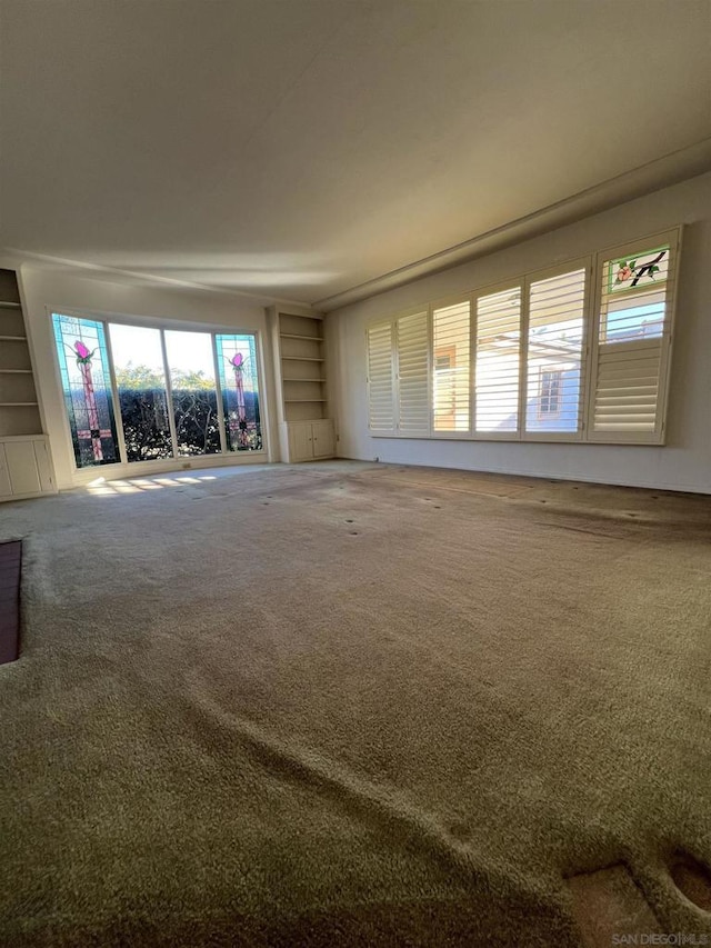 unfurnished living room featuring built in shelves and carpet flooring