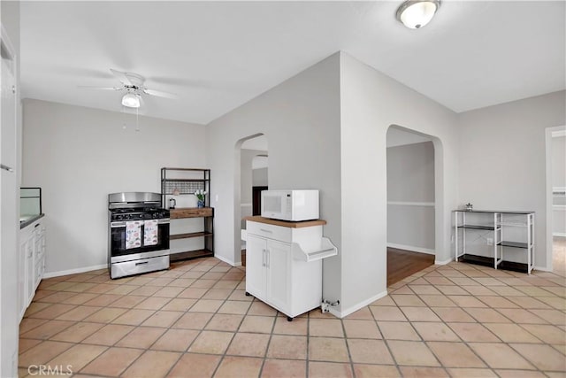 kitchen featuring light tile patterned floors, white cabinets, gas range, and ceiling fan