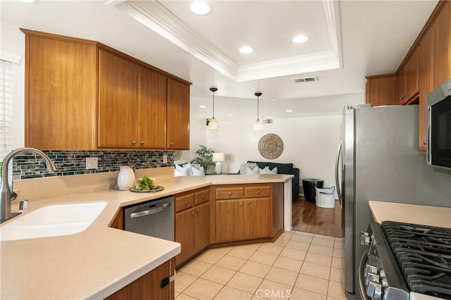 kitchen with kitchen peninsula, pendant lighting, appliances with stainless steel finishes, sink, and a tray ceiling