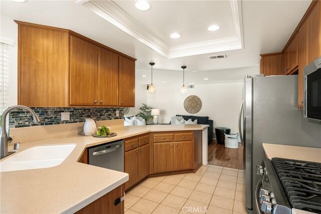 kitchen featuring kitchen peninsula, sink, decorative light fixtures, a tray ceiling, and stainless steel appliances