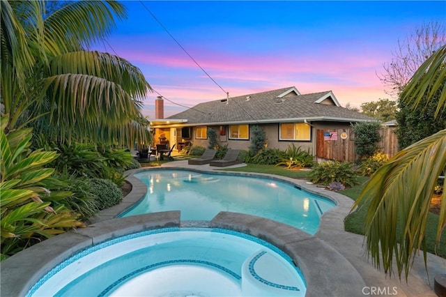 pool at dusk with a patio area and an in ground hot tub