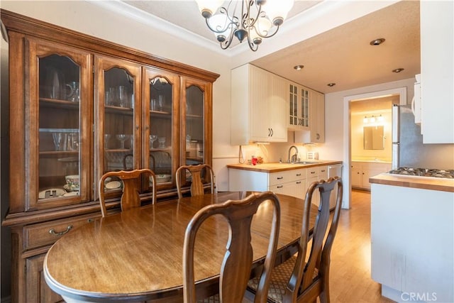 dining room featuring an inviting chandelier, ornamental molding, sink, and light hardwood / wood-style floors