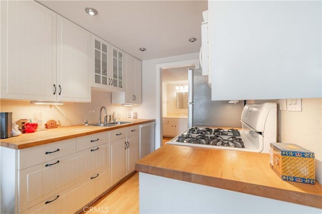 kitchen with stainless steel appliances, white cabinetry, sink, and butcher block counters