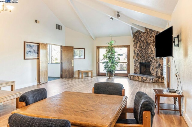 dining room featuring light hardwood / wood-style flooring, beamed ceiling, high vaulted ceiling, and a stone fireplace