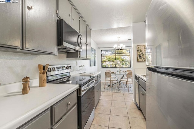 kitchen featuring appliances with stainless steel finishes, gray cabinetry, light tile patterned floors, a textured ceiling, and a notable chandelier