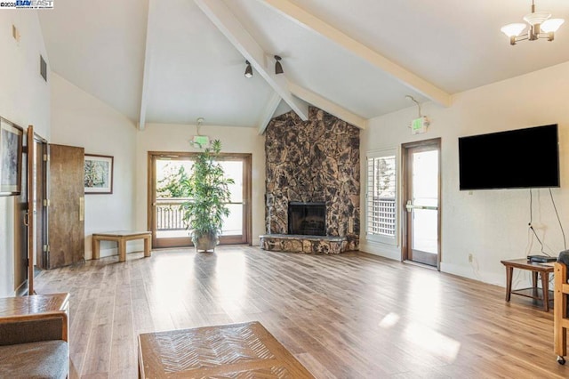 unfurnished living room with light hardwood / wood-style flooring, a wealth of natural light, vaulted ceiling with beams, and a stone fireplace