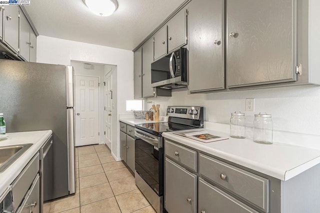 kitchen with light tile patterned floors, appliances with stainless steel finishes, and gray cabinetry