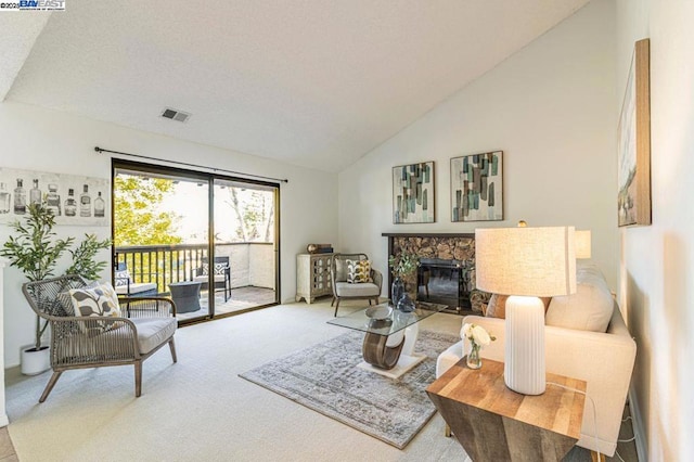 carpeted living room with a stone fireplace and lofted ceiling