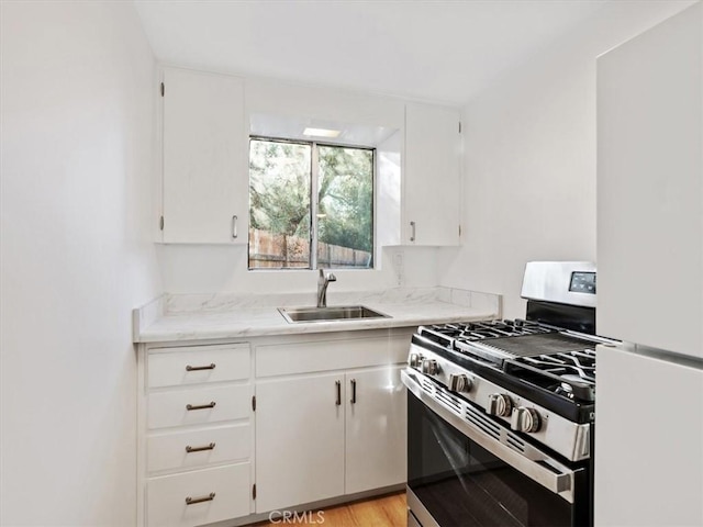 kitchen with stainless steel gas stove, white cabinets, a sink, and freestanding refrigerator