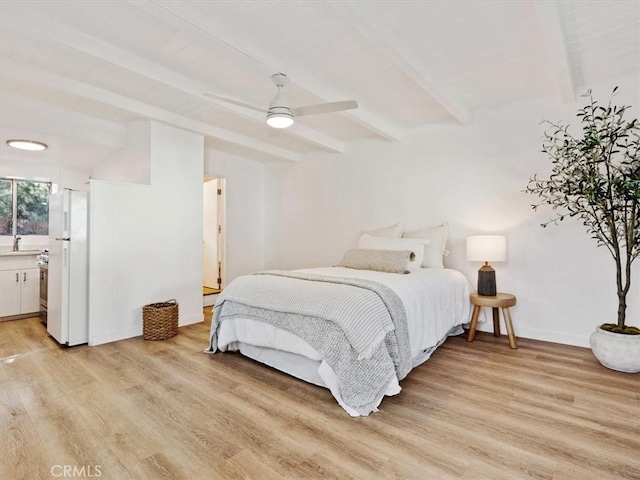 bedroom featuring baseboards, freestanding refrigerator, beam ceiling, light wood-style floors, and a sink