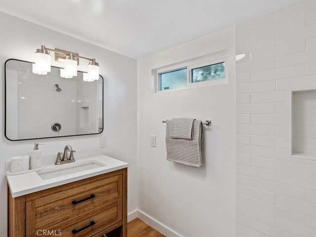 bathroom with baseboards, wood finished floors, tiled shower, and vanity