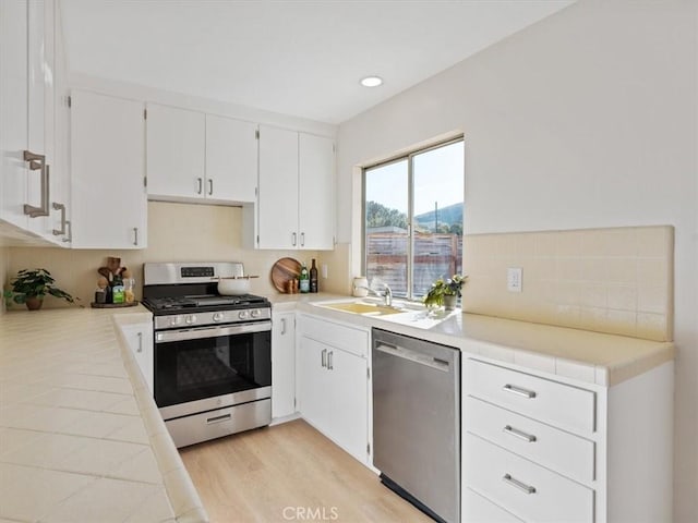 kitchen featuring light wood-style flooring, stainless steel appliances, a sink, white cabinetry, and light countertops