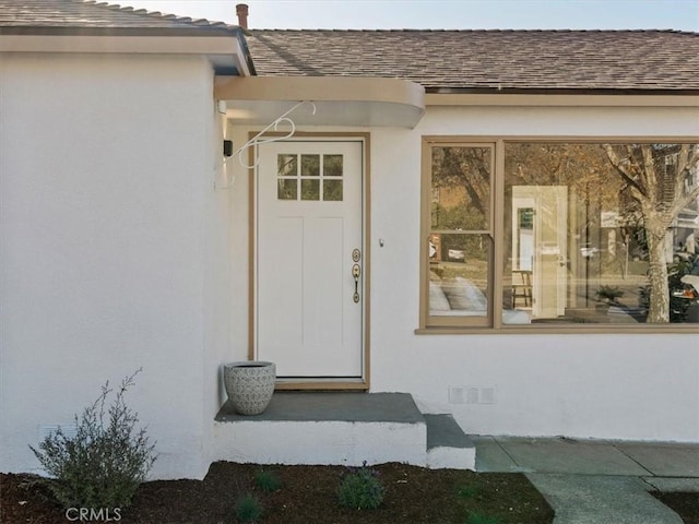 view of exterior entry featuring crawl space, a shingled roof, and stucco siding