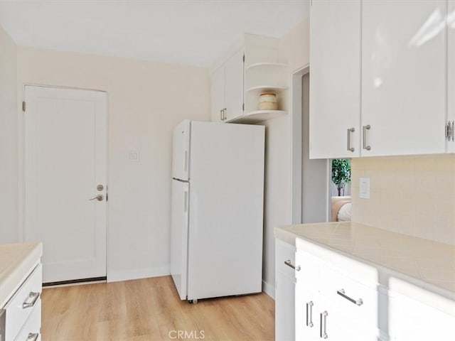 kitchen with open shelves, light wood-style floors, freestanding refrigerator, and white cabinetry