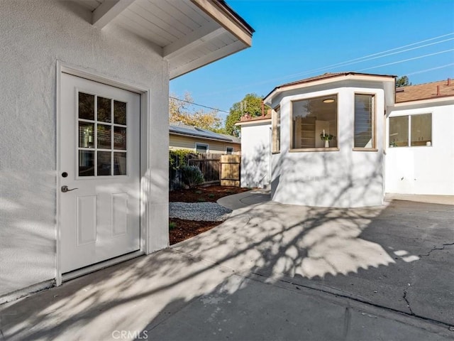 view of exterior entry with fence and stucco siding