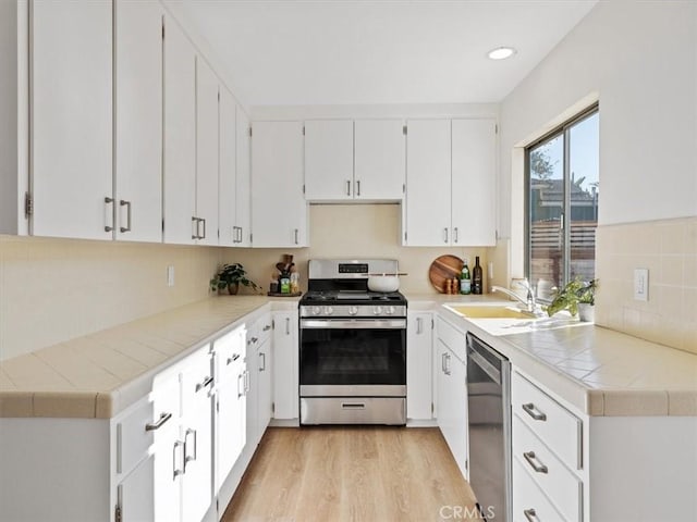 kitchen with stainless steel appliances, a sink, white cabinets, decorative backsplash, and light wood finished floors