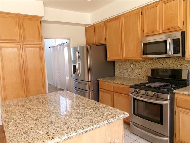 kitchen featuring light stone countertops, light tile patterned floors, a kitchen island, backsplash, and stainless steel appliances