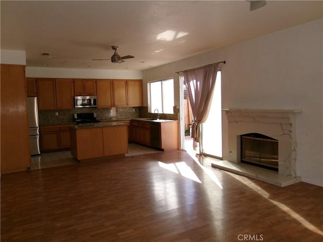 kitchen with a center island, stainless steel appliances, decorative backsplash, light wood-type flooring, and ceiling fan