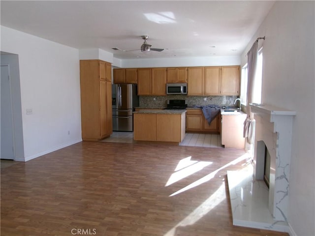 kitchen with ceiling fan, sink, backsplash, light wood-type flooring, and stainless steel appliances