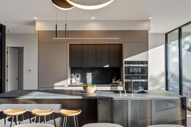 kitchen with double oven, decorative backsplash, sink, dark brown cabinetry, and a breakfast bar area