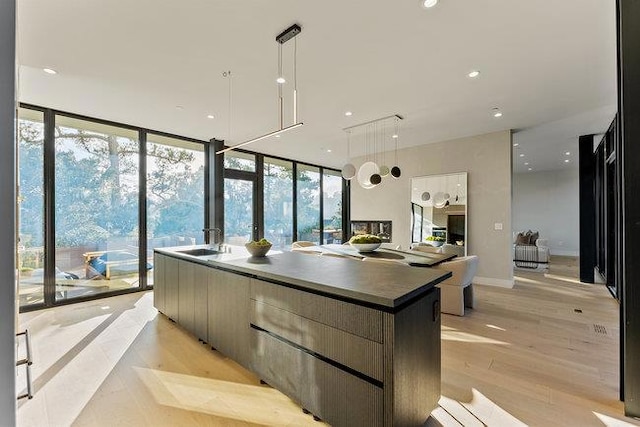 kitchen with a wall of windows, sink, hanging light fixtures, a large island, and light wood-type flooring