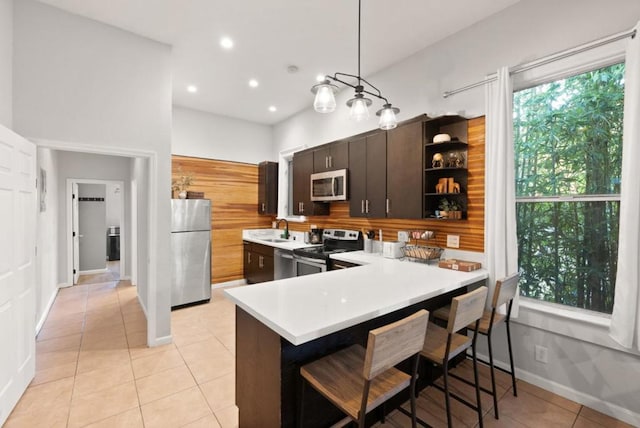 kitchen with pendant lighting, dark brown cabinetry, stainless steel appliances, and kitchen peninsula